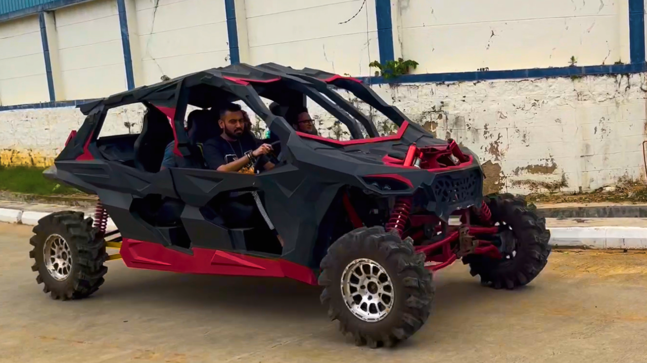 A man steers a red and black Arav, 4 seater, 4x4 off road vehicle , riding on a smooth road.